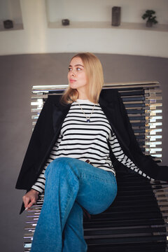 Attractive blonde woman relaxing in stylish oversized blazer on chrome designer daybed in modern interior