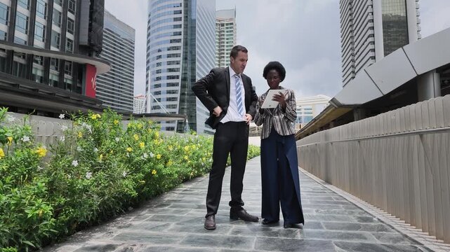 Couple walking hand in hand along a city path with greenery and modern skyscrapers in the background