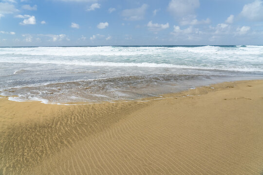 View of the sandy beach with rolling ocean waves under a blue sky in Cofete, Canary Islands, Spain.