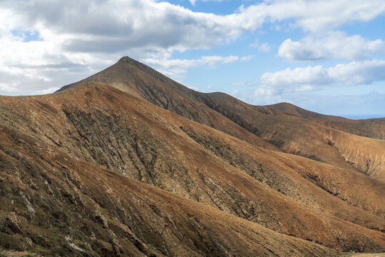 View of the rugged volcanic mountain landscape of Fuerteventura under a bright blue sky with scattered clouds in Pajara, Canary Islands, Spain.
