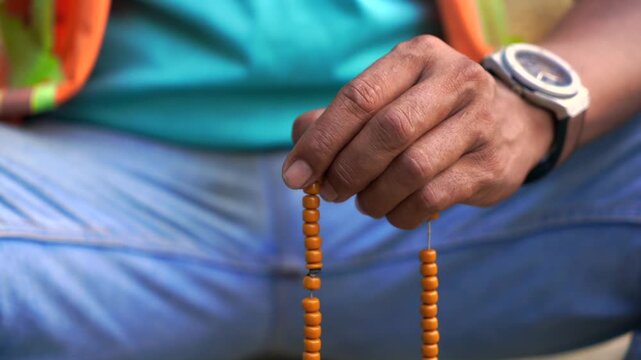 Hand Holding Prayer Beads for Islamic Dhikr
Close-up of a Muslim man's hand holding traditional wooden prayer beads (tasbih) while performing dhikr and Islamic prayer in a peaceful setting.