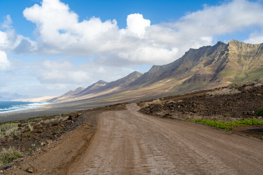 View of the rugged dirt road leading towards the dramatic mountains and coastline of Cofete, Canary Islands, Spain.