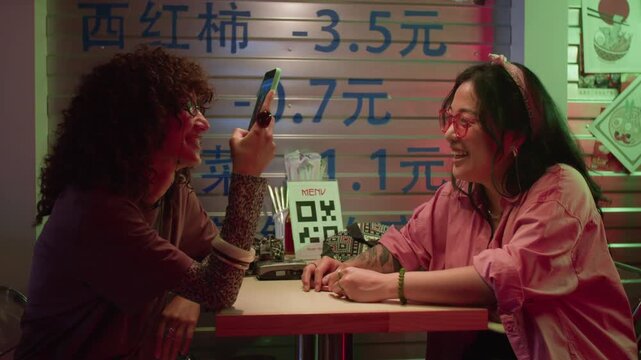 Diverse young adult women recording video on smartphone while meeting up at Asian restaurant. Footage is suitable for digital dining, contactless ordering, and mobile technology campaigns