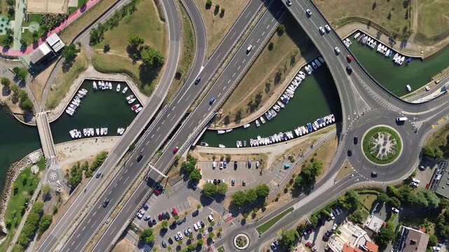 Top down aerial view of a road interchange with a roundabout, moving traffic and a waterway in Koper, Slovenia, revealing modern urban infrastructure from above.