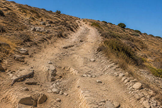 Steep unpaved trail on dry rocky hillside with ruts and exposed roots, arduous hiking path concept