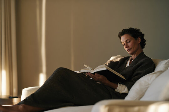 A serene moment captured as a woman enjoys reading a book in a cozy setting, bathed in warm natural light, embodying tranquility and reflection.