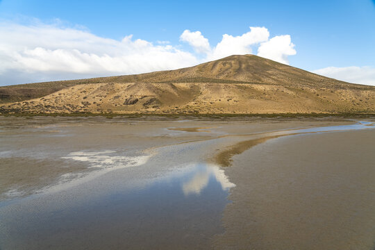 View of the volcanic landscape with tidal flats and reflections in the water under a clear blue sky in Jandia, Canarias, Spain.