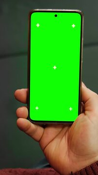 Vertical video of male hand holding smartphone with green screen chroma key and tracking markers crosses. Close up of man using mobile phone template mockup blank display for app design tracking