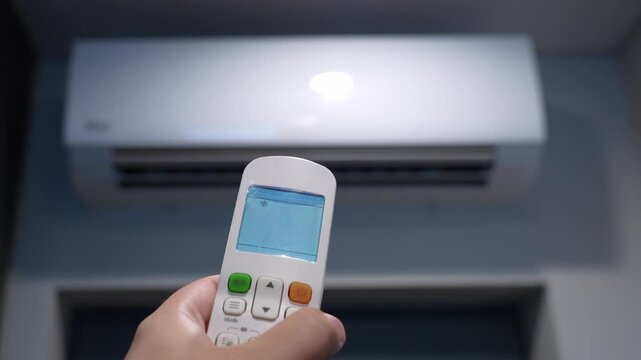 Hand pressing off button on air conditioner remote with blurred AC in background