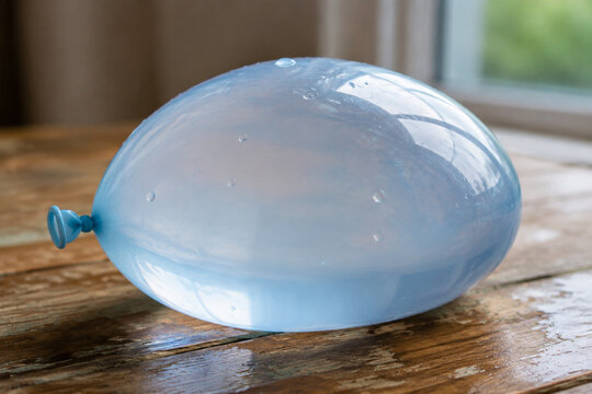 Overfilled translucent water balloon on wooden table, tension and fragility concept