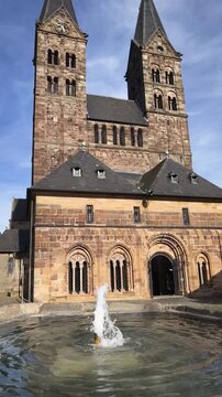 Dom St. Peter in Fritzlar: Au&szlig;enansicht der romanischen Kathedrale mit den markanten Doppelt&uuml;rmen und dem Springbrunnen im Vordergrund an einem sonnigen Tag in Hessen, Deutschland.
