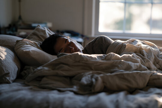 A young woman sleeps peacefully in a comforting bed, surrounded by soft pillows and blankets, creating a serene atmosphere that evokes relaxation and deep rest.