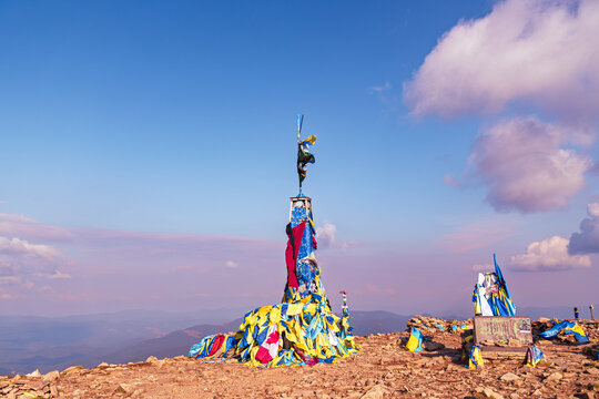 Carpathian mountain peak, Mount Hoverla, with a large cluster of colorful prayer flags and ribbons fluttering in the wind under a vibrant blue and pink sunset sky