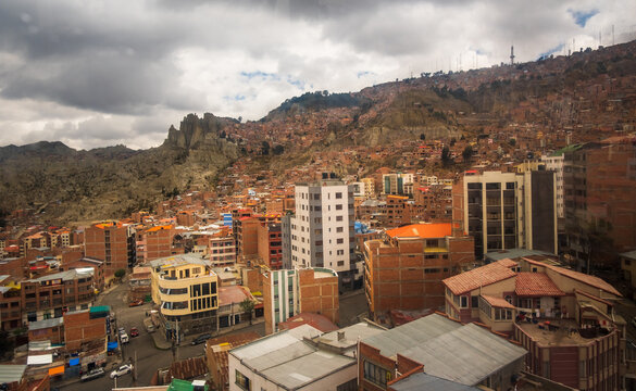 View of the sprawling cityscape of La Paz, with dense brick buildings climbing the steep Andean hillsides under a cloudy sky in La Paz, La Paz Department, Bolivia.