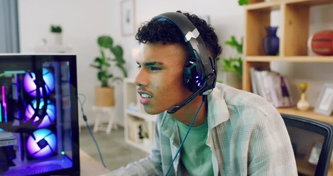 A concentrated gamer playing a video game on his computer monitor with latest headset gear. Young trendy guy playing esports on multiplayer mode and challenging his components via a microphone