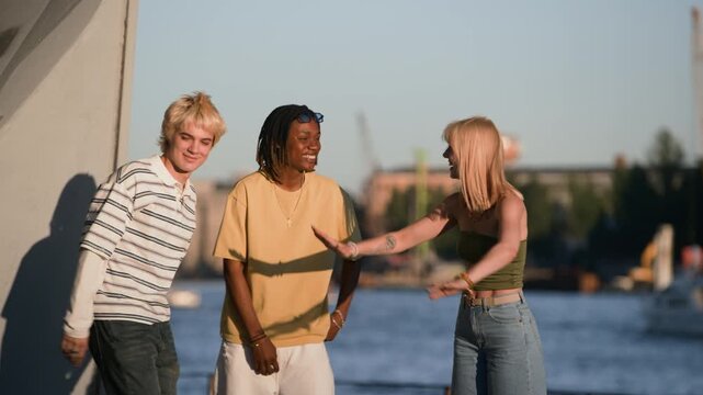Multiethnic teenagers giving high fives and laughing outdoors near river. Clip is ideal for youth lifestyle commercials, diversity campaigns, and social connection advertisements