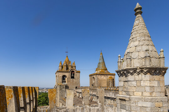 View of the Cathedral of Evora with its historic stone towers, spires, and crenellated walls under a clear blue sky in Evora, Distrito de Evora, Portugal.