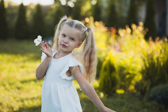 a cute five-year-old girl in a white dress is playing in a green summer garden. happy childhood