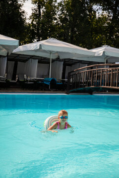 Young girl floating with inflatable ring in wide blue resort swimming pool. Concept of family hotels, beginner swimming and summer travel.