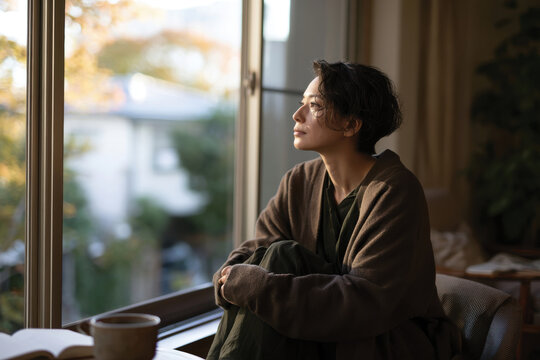 A contemplative woman gazes out the window, lost in thought as soft natural light filters through, evoking feelings of introspection and calm.