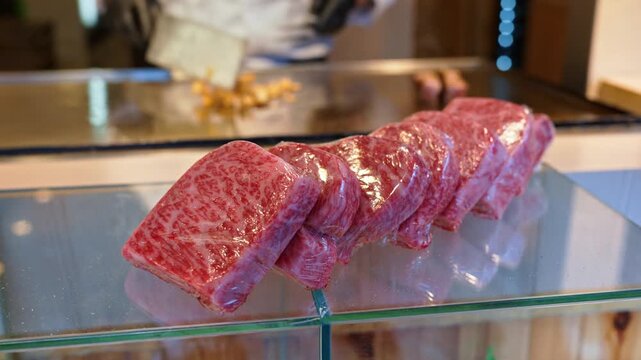 Fresh wagyu beef steaks vacuum sealed on glass counter with professional chef cooking in background.
