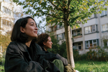 Fototapeta premium A serene scene of two friends enjoying momentary peace together while seated under a tree in an urban park, showcasing friendship and tranquility.