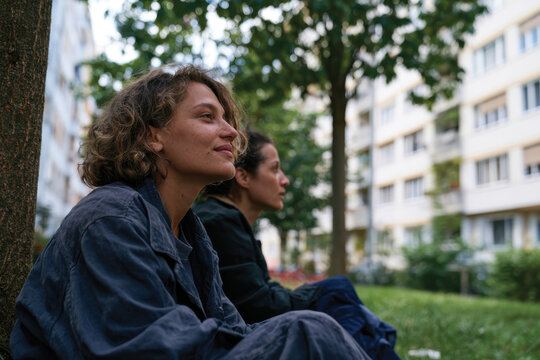 A peaceful moment shared between two women resting under a tree in the city, emphasizing the importance of nature and companionship in a busy world.