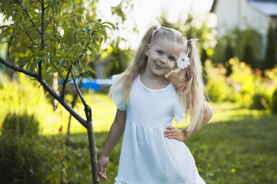 a cute five-year-old girl in a white dress is playing in a green summer garden. happy childhood