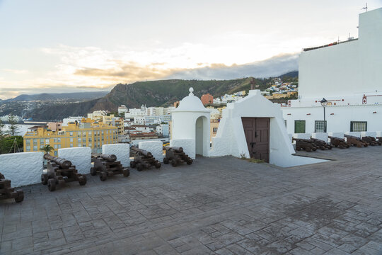 View of historic cannons on the stone ramparts of Castillo de Santa Catalina overlooking the coastal town and mountains in Santa Cruz de La Palma, Canary Islands, Spain.