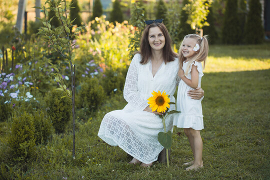 a cute five-year-old girl with mother in a white dress are playing in a green summer garden. happy childhood