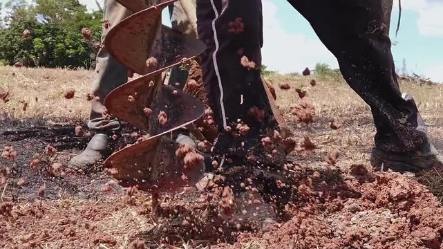 Close-up of an industrial auger drilling a deep hole into the soil for construction or agricultural purposes. The spiral blade spins, digging up dirt