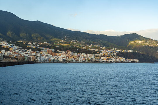 View of the coastal town of Santa Cruz de La Palma nestled against lush green mountains under a clear blue sky in Santa Cruz de La Palma, Canary Islands, Spain.