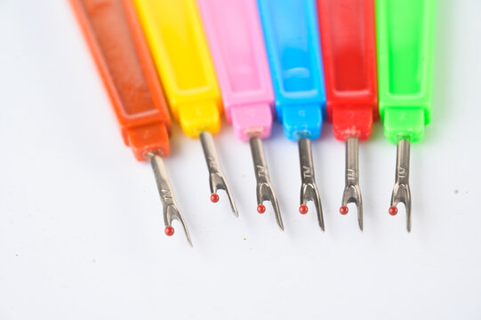 Colorful seam rippers lined up on a white background, each with a plastic handle in different bright colors.