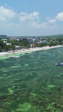 Vertical drone approaches and pans left over Alona Beach, showing reef waters, white sand, boats, and beachfront buildings in Panglao, Bohol