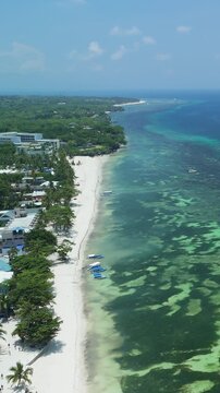 Vertical drone ascends and pulls back over Alona Beach, revealing white sand, reef waters, boats, and the Panglao coastline in Bohol