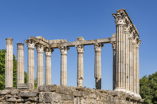View of the ancient Roman Temple of Evora with its iconic Corinthian columns standing against a clear blue sky in Evora, Distrito de Evora, Portugal.
