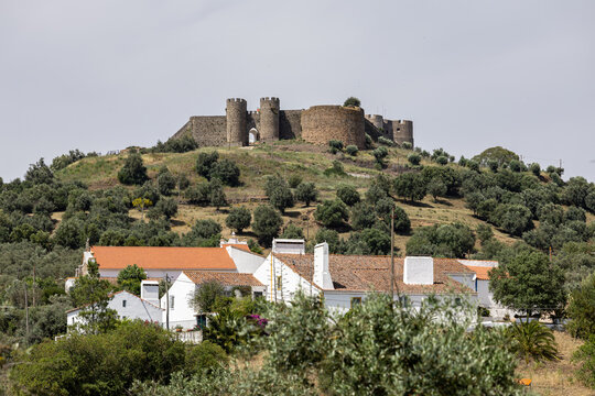 View of the historic Castle of Evoramonte perched on a hilltop overlooking the surrounding olive groves and traditional white houses in Evoramonte, Evora District, Portugal.