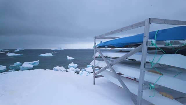 Kayaks stacked by snowy shore in Nuuk with drifting sea ice under cloudy sky