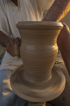 View of a skilled potter shaping a clay vessel on a spinning wheel with hands covered in mud in Multan City, Punjab, Pakistan.