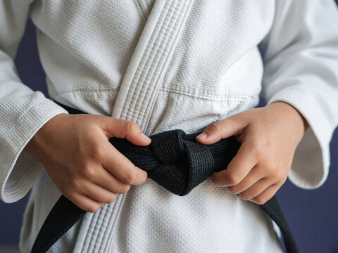 Close up of hands adjusting a black belt on a white martial arts gi. Traditional judo or karate uniform texture. Discipline and preparation concept