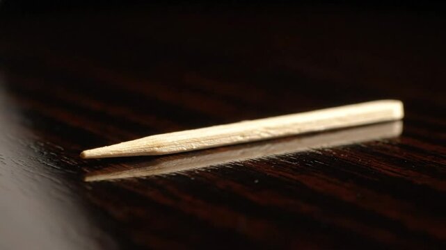 Close-up of a single wooden toothpick resting on a dark, glossy wooden surface with reflection
