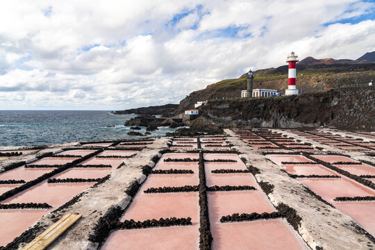 View of Salinas de Fuencaliente with pink salt pans, volcanic rock borders, and the red and white lighthouse in Santa Cruz de La Palma, Canarias, Spain.