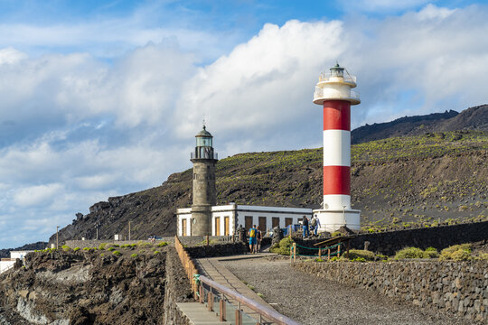 View of the historic and modern lighthouses at Salinas de Fuencaliente set against a dramatic volcanic landscape with people walking along the path in Santa Cruz de La Palma, Canarias, Spain.