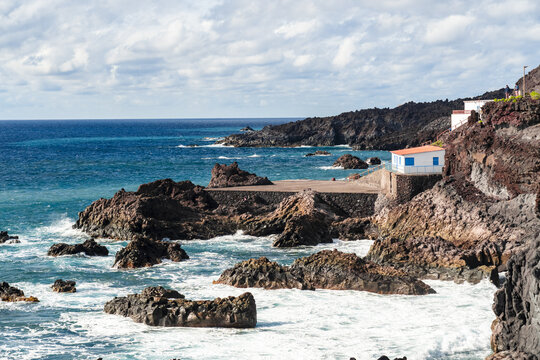 View of the volcanic coastline at Salinas de Fuencaliente with dark rocks, crashing waves, and a small building overlooking the Atlantic Ocean in Santa Cruz de La Palma, Canarias, Spain.