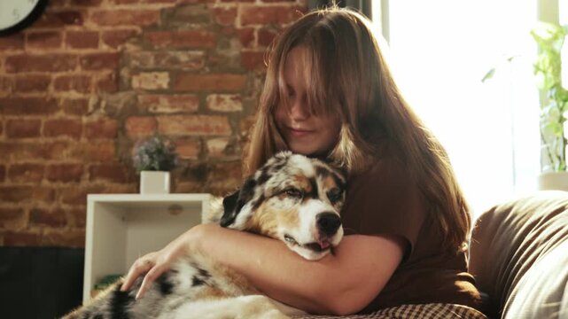 Woman hugs affectionate Australian Shepherd while relaxing together on sofa. Concept of pet bonding, emotional support, animal friendship, and home lifestyle.