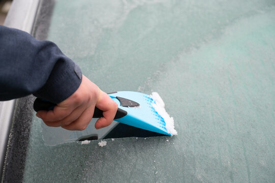 Driver is removing snow from car windshield with ice scraper and broom, clean car window from icy frost, winter season