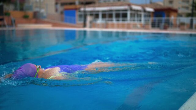 Female swimmer performing powerful backstroke in outdoor pool, demonstrating graceful swimming technique, athletic performance, endurance and professional training.