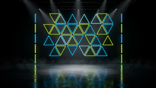 : A dark stage backdrop features glowing neon yellow and blue triangular patterns illuminated by spotlights and mist.