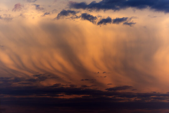 View of dramatic sunset clouds with golden and orange hues streaking across the sky above Jahanian, Punjab, Pakistan.