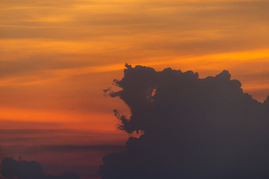 View of a vibrant sunset with dark, dramatic clouds silhouetted against an intense orange and golden sky in Jahanian, Punjab, Pakistan.